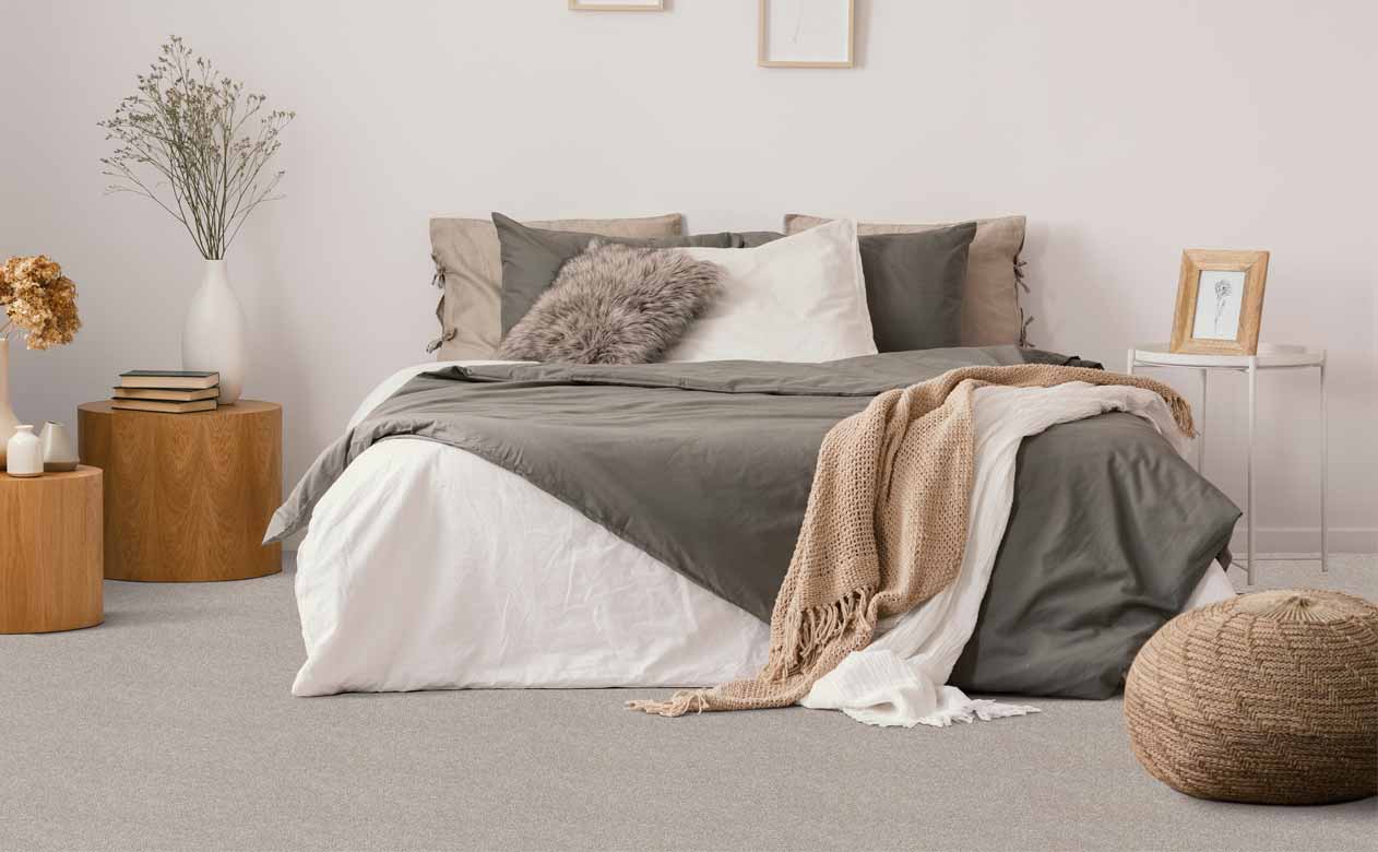 bedroom with wood tables, plants, and cozy layered bed with plush gray carpet