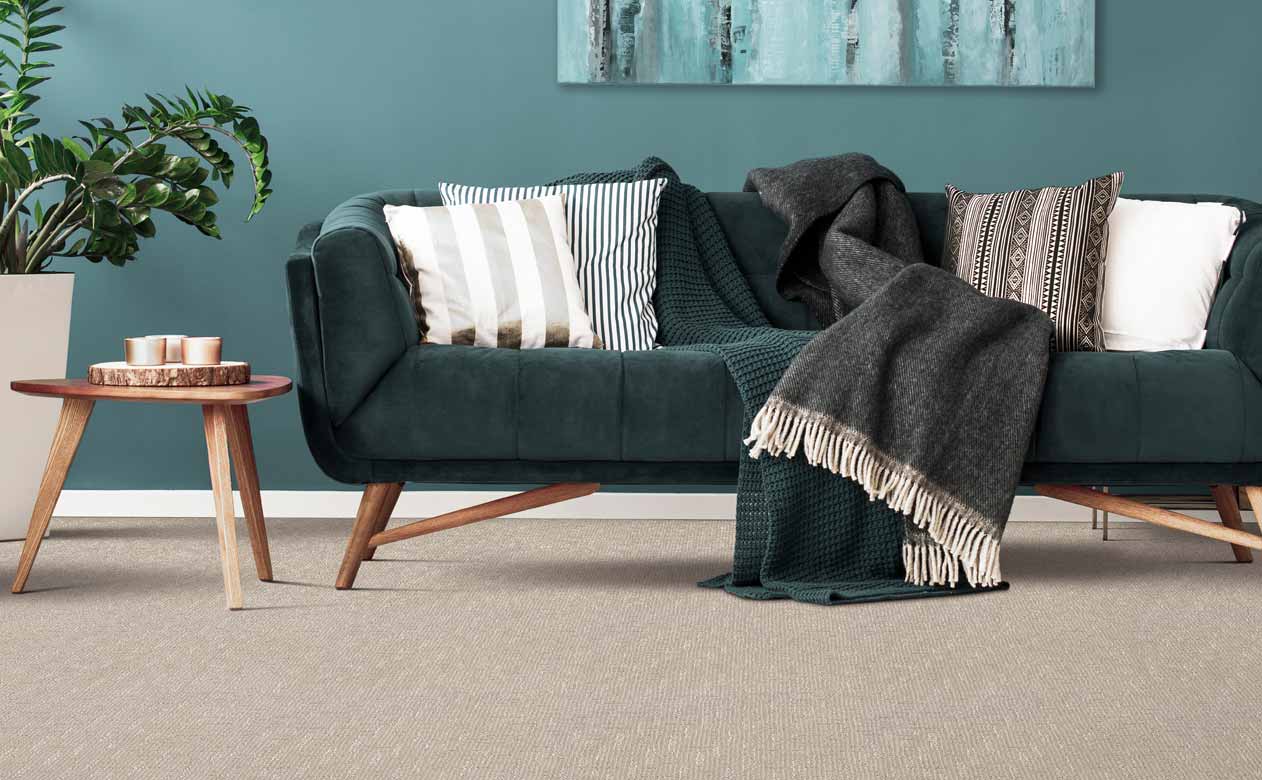 living room with blue accent wall, green couch and wood accents, textured beige carpeted floor