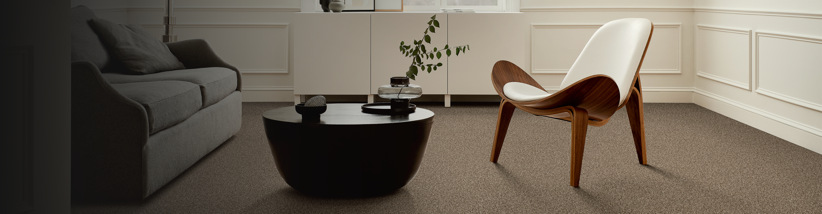 Modern living room with gray couch, white modern chair and black coffee table, carpeted in beige carpet